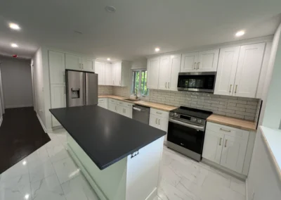 Modern kitchen with white cabinets, dark countertop, stainless steel appliances, and subway tile backsplash, featuring natural light from windows.