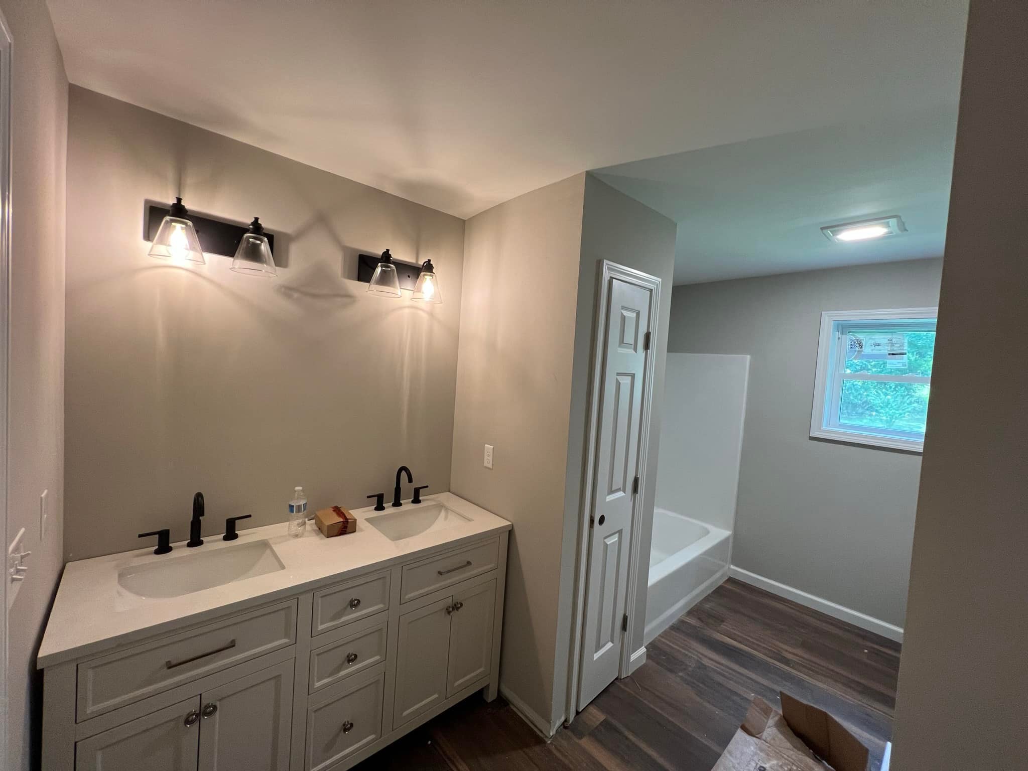 Bathroom remodel in Tolland County CT with double vanity, black fixtures, and new bathtub with modern lighting.