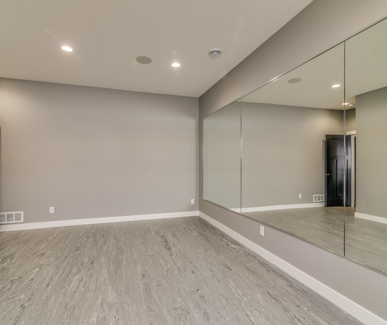 Finished basement in Tolland County CT with gray vinyl flooring, recessed lighting, and large wall mirror.